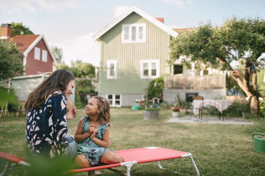 Mor og datter sitter på en solseng i en hage utenfor en hus